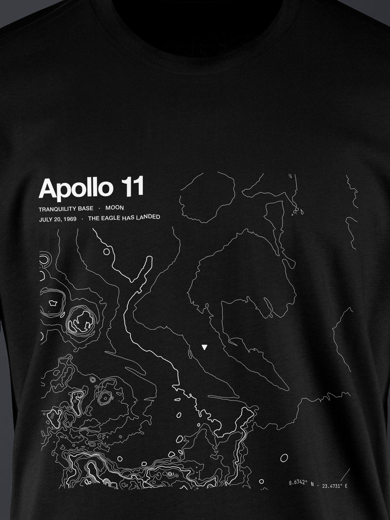 Topographic contour t-shirt of Apollo 11, Mare Tranquillitatis (Tranquility Base), the Moon, the July 20, 1969 landing site, rendered from NASA LRO LOLA laser altimetry. Cotton contour-art tee by Horizon Editions - real terrain, hand-drawn, no AI.